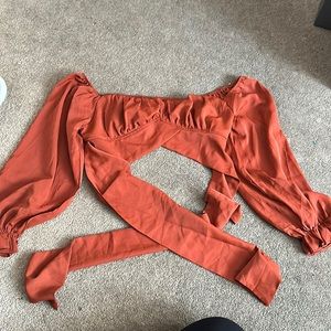 Rusty orange color. Ties in the front with ruffle sleeves